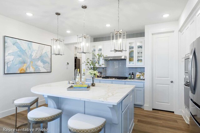 kitchen with decorative backsplash, decorative light fixtures, a center island with sink, and white cabinetry