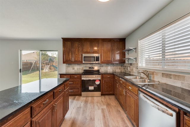 kitchen featuring stainless steel appliances, tasteful backsplash, dark stone countertops, sink, and light hardwood / wood-style floors