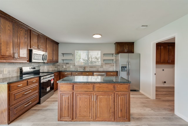 kitchen featuring a center island, stainless steel appliances, light hardwood / wood-style floors, dark stone counters, and backsplash