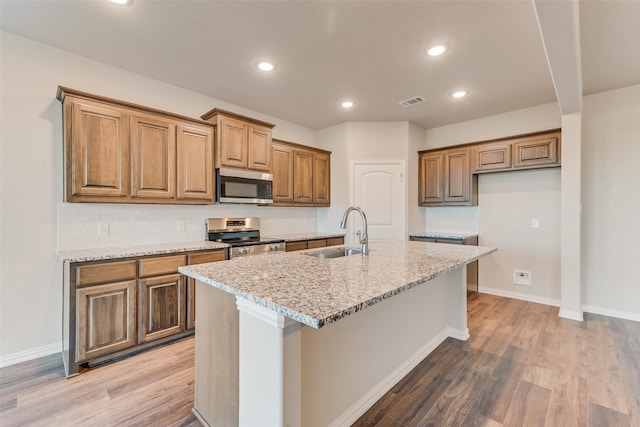 kitchen with light stone countertops, appliances with stainless steel finishes, a center island with sink, and sink