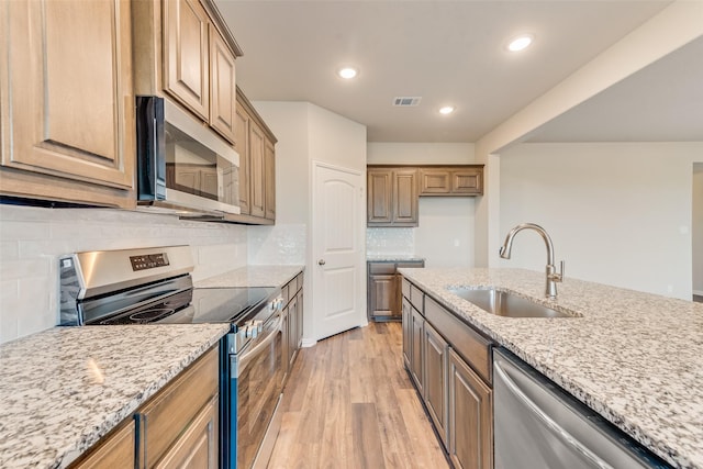 kitchen with light stone countertops, stainless steel appliances, decorative backsplash, sink, and light hardwood / wood-style flooring