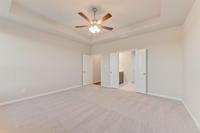 unfurnished bedroom with ceiling fan, ensuite bath, light carpet, and a tray ceiling