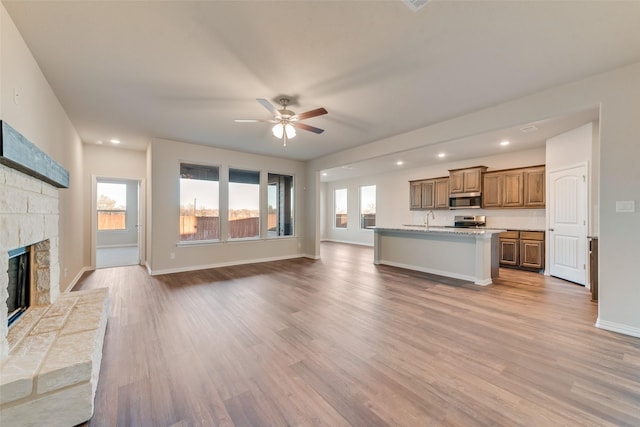 unfurnished living room with ceiling fan, sink, light hardwood / wood-style flooring, and a stone fireplace