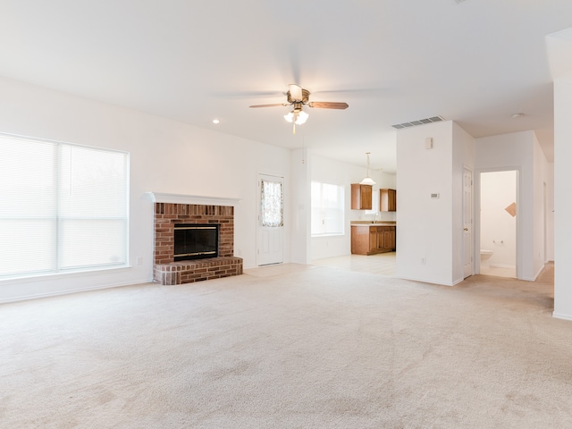 unfurnished living room featuring a brick fireplace, light colored carpet, and ceiling fan