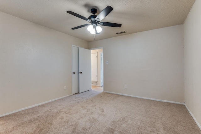 spare room featuring light carpet, ceiling fan, and a textured ceiling