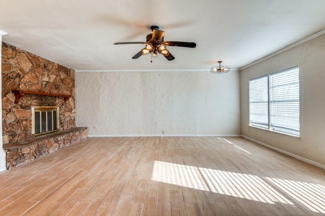 unfurnished living room featuring ceiling fan, a stone fireplace, ornamental molding, and light hardwood / wood-style flooring