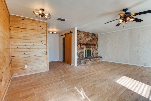 unfurnished living room featuring a barn door, a fireplace, wood walls, and hardwood / wood-style floors