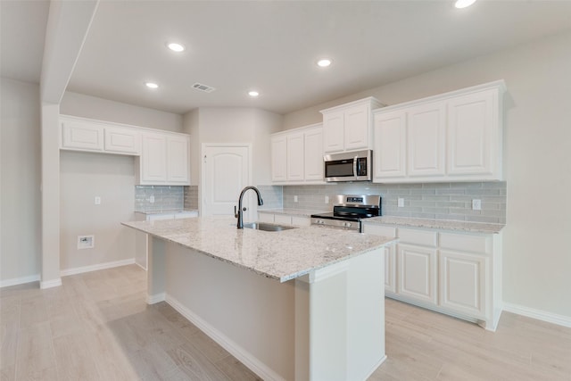 kitchen with white cabinetry, stainless steel appliances, an island with sink, sink, and light stone counters