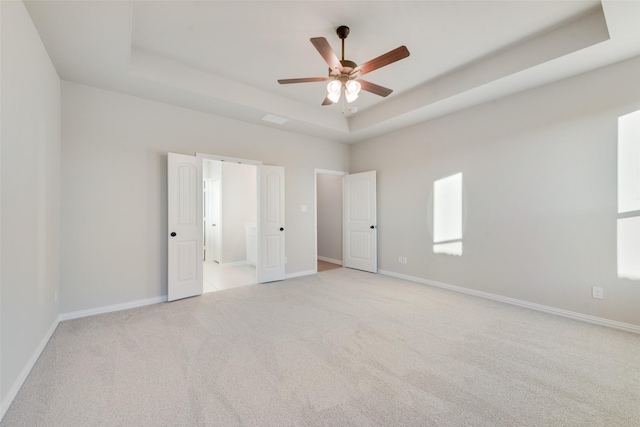 unfurnished bedroom with light carpet, ceiling fan, and a tray ceiling