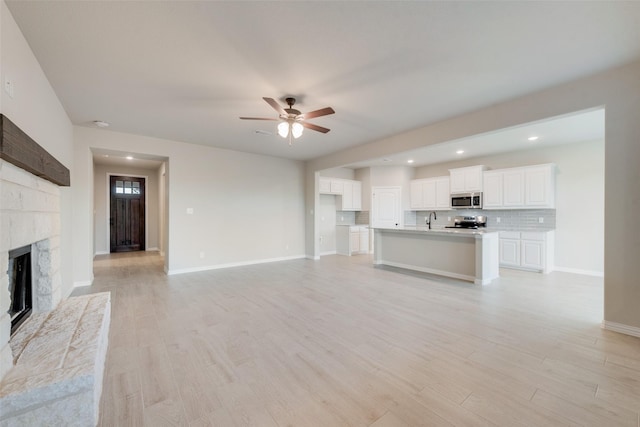 unfurnished living room with ceiling fan, sink, light hardwood / wood-style flooring, and a tiled fireplace