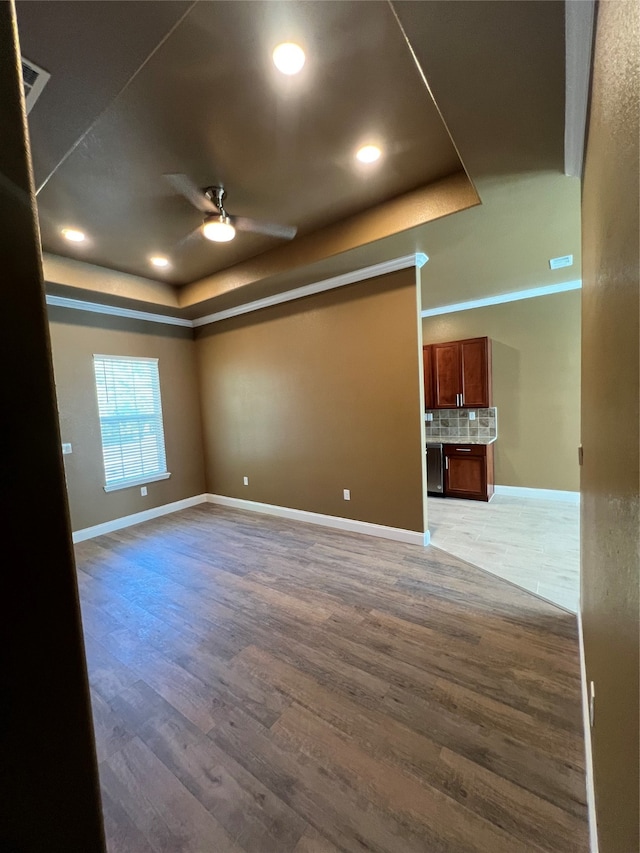 empty room with a tray ceiling, hardwood / wood-style flooring, and ceiling fan