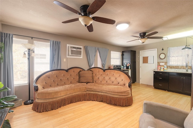 living room with an AC wall unit, a textured ceiling, and light wood-type flooring