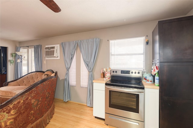 kitchen with light hardwood / wood-style flooring, stainless steel electric range, an AC wall unit, ceiling fan, and white cabinets