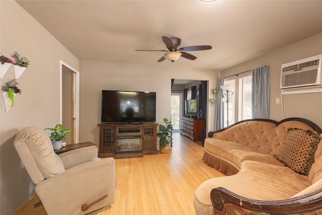 living room featuring a wall mounted air conditioner, light hardwood / wood-style flooring, and ceiling fan