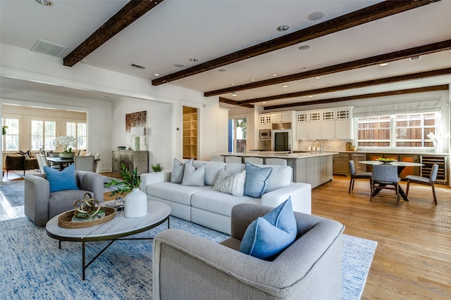 living room featuring beverage cooler, beam ceiling, light hardwood / wood-style floors, and sink