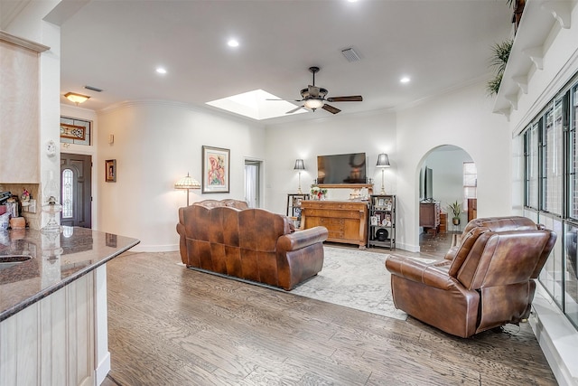 living room featuring ceiling fan, hardwood / wood-style flooring, ornamental molding, and a skylight