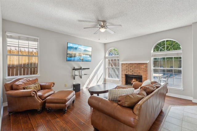 living room with ceiling fan, wood-type flooring, a textured ceiling, and a brick fireplace