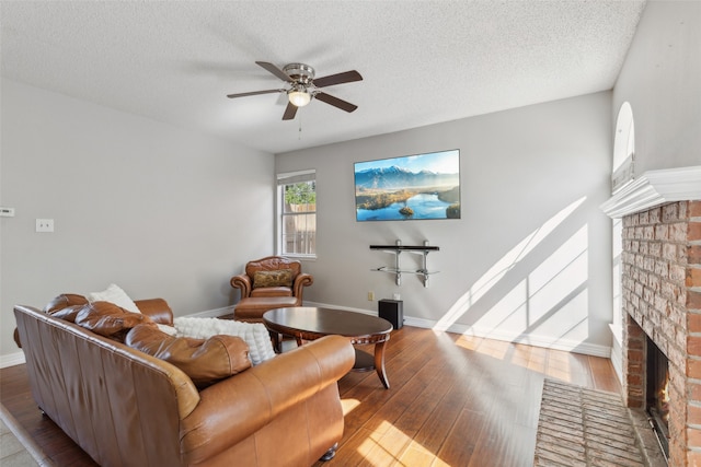 living room with light hardwood / wood-style flooring, a brick fireplace, a textured ceiling, and ceiling fan