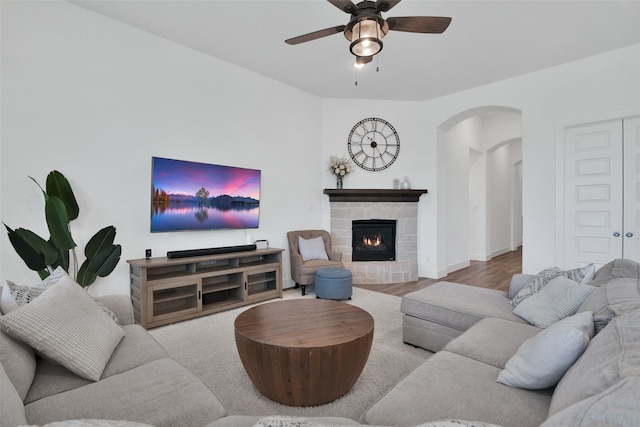 living room with a stone fireplace, light hardwood / wood-style flooring, and ceiling fan