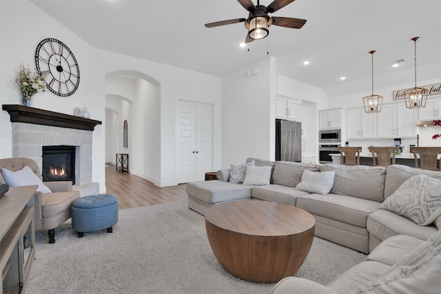 living room with a stone fireplace, light hardwood / wood-style flooring, and ceiling fan