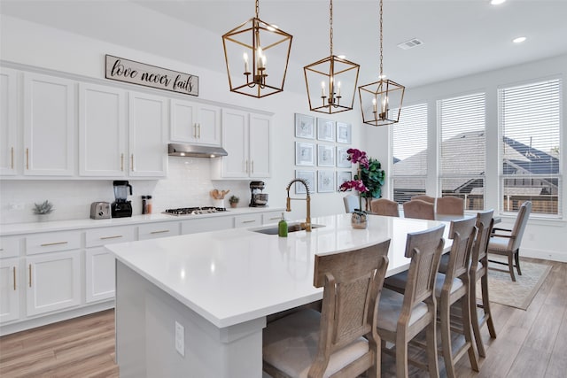 kitchen with a center island with sink, sink, white cabinets, and pendant lighting