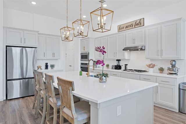 kitchen with appliances with stainless steel finishes, a kitchen island with sink, sink, and hanging light fixtures