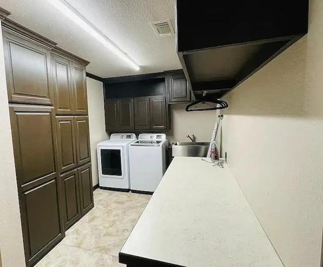 clothes washing area with cabinets, sink, independent washer and dryer, and a textured ceiling