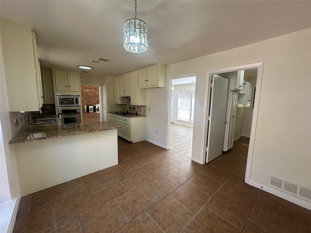 kitchen featuring kitchen peninsula, a chandelier, pendant lighting, stainless steel appliances, and stone counters