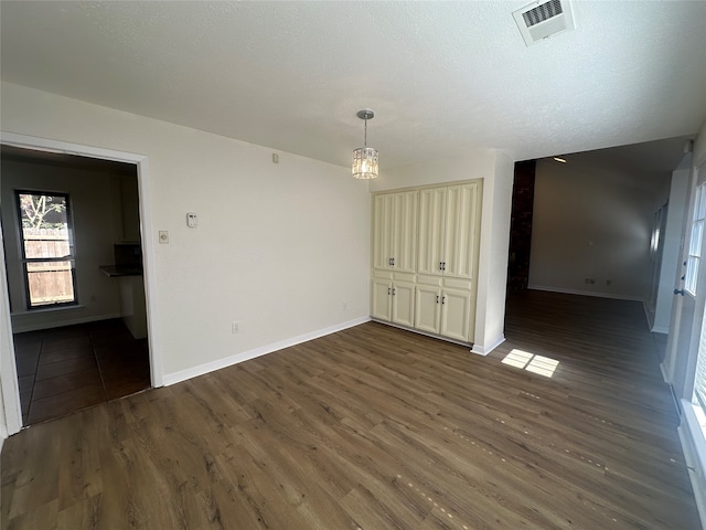 spare room with a notable chandelier, dark wood-type flooring, and a textured ceiling