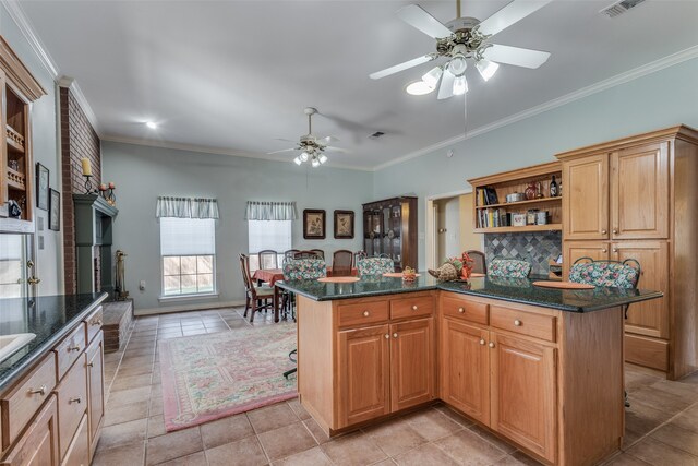 kitchen with a kitchen bar, a kitchen island, ornamental molding, light tile patterned flooring, and dark stone counters