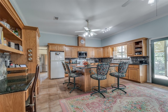 kitchen featuring a breakfast bar area, appliances with stainless steel finishes, ceiling fan, a kitchen island with sink, and decorative backsplash