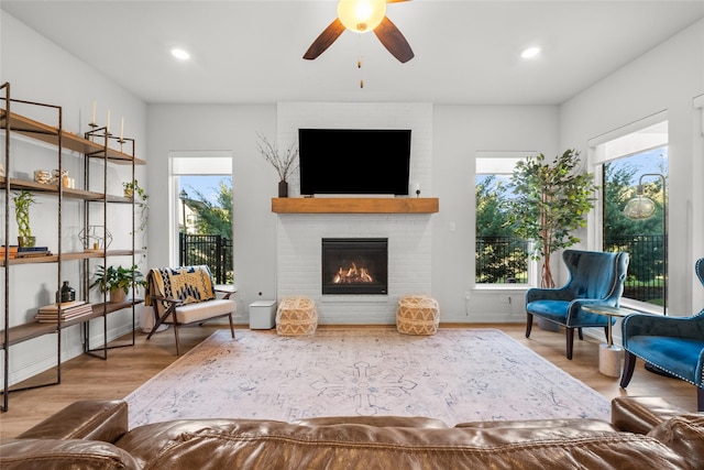 sitting room featuring ceiling fan, wood-type flooring, and a brick fireplace