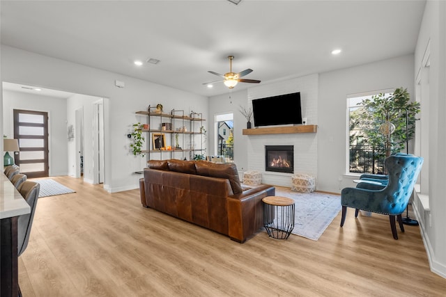 living room with light wood-type flooring, a brick fireplace, and ceiling fan