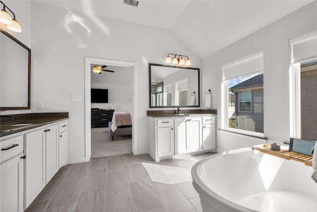 bathroom with ceiling fan, a washtub, vanity, and vaulted ceiling