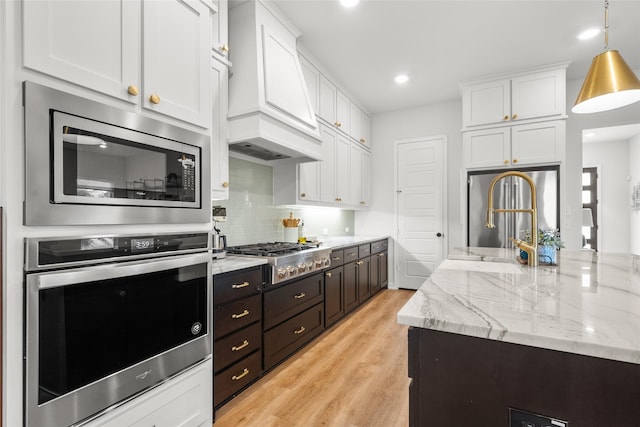 kitchen featuring custom exhaust hood, stainless steel appliances, light hardwood / wood-style flooring, white cabinetry, and hanging light fixtures