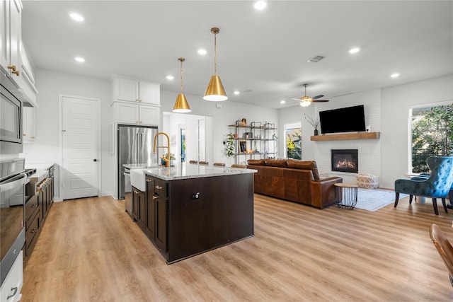 kitchen with white cabinetry, decorative light fixtures, a kitchen island with sink, a fireplace, and dark brown cabinets