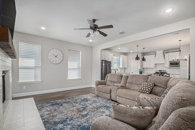 living room featuring ceiling fan with notable chandelier, sink, a brick fireplace, and dark hardwood / wood-style floors