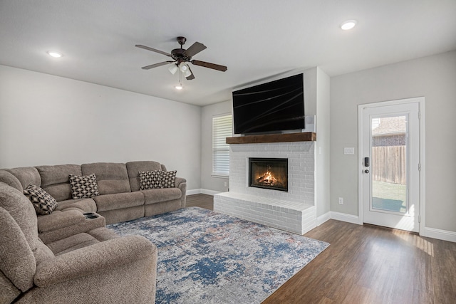 living room with a brick fireplace, dark hardwood / wood-style floors, and ceiling fan