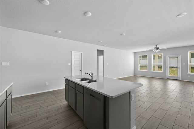 kitchen with ceiling fan, sink, a kitchen island with sink, dishwasher, and gray cabinets