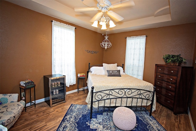 bedroom featuring ceiling fan, wood-type flooring, a tray ceiling, and multiple windows