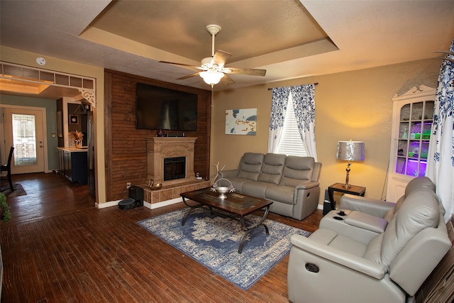 living room with a raised ceiling, dark hardwood / wood-style floors, and ceiling fan