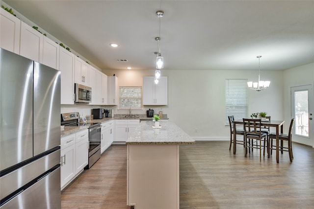 kitchen with a kitchen island, light stone countertops, stainless steel appliances, pendant lighting, and white cabinetry