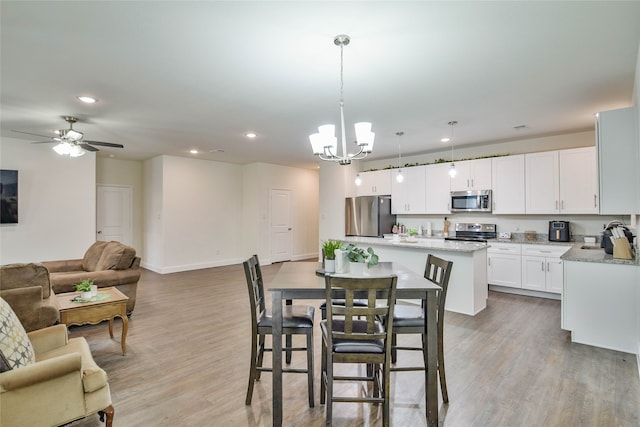 dining room with ceiling fan with notable chandelier and light hardwood / wood-style floors