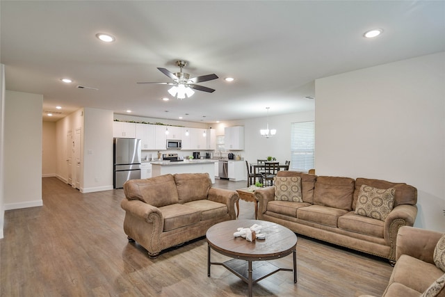 living room with ceiling fan with notable chandelier and light wood-type flooring