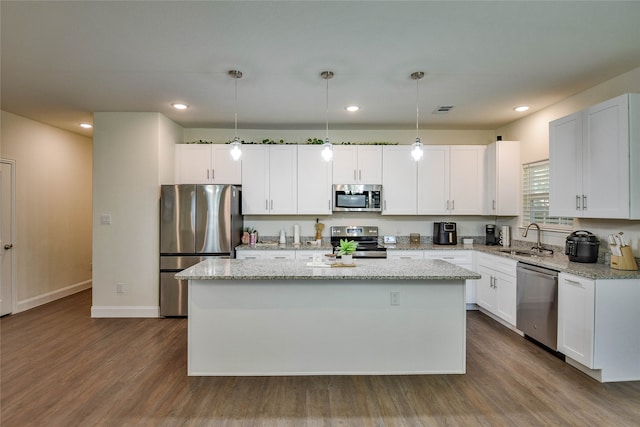 kitchen with decorative light fixtures, stainless steel appliances, white cabinetry, and a kitchen island