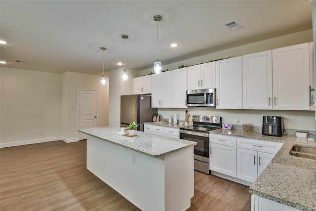 kitchen with white cabinets, hanging light fixtures, appliances with stainless steel finishes, a center island, and light wood-type flooring