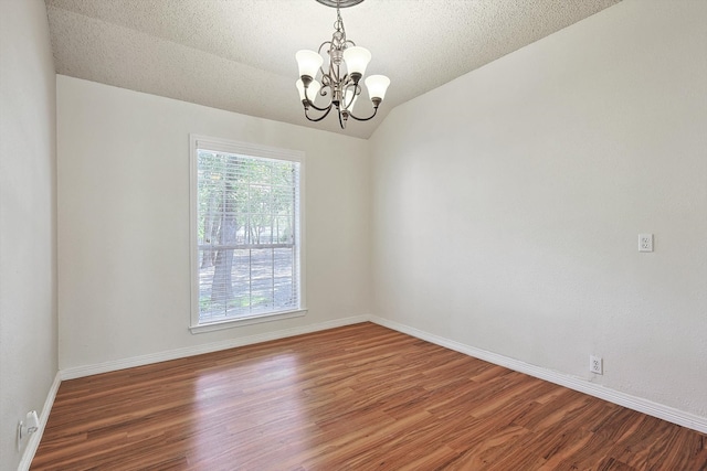 empty room featuring wood-type flooring, vaulted ceiling, a notable chandelier, and a textured ceiling