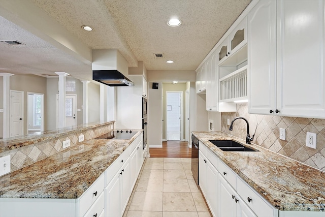 kitchen with light stone counters, white cabinets, sink, black appliances, and decorative columns