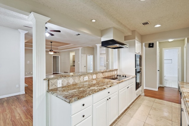 kitchen featuring light wood-type flooring, ornate columns, black electric stovetop, light stone countertops, and white cabinetry