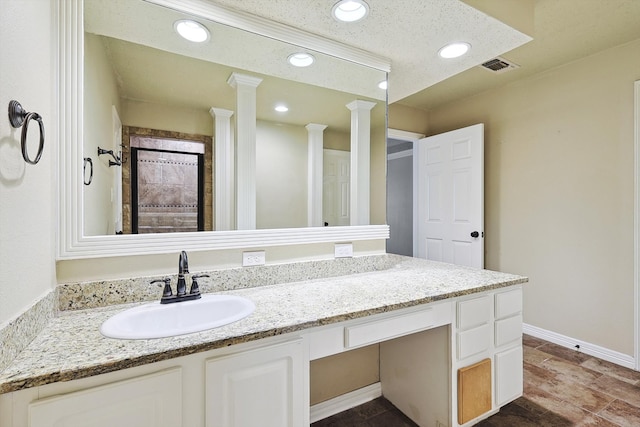 bathroom with ornate columns, vanity, and a textured ceiling